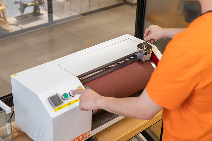 A quality inspector conducts a wear test on the sole of a shoe.