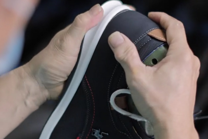 A worker meticulously glues the upper and sole of a shoe together.